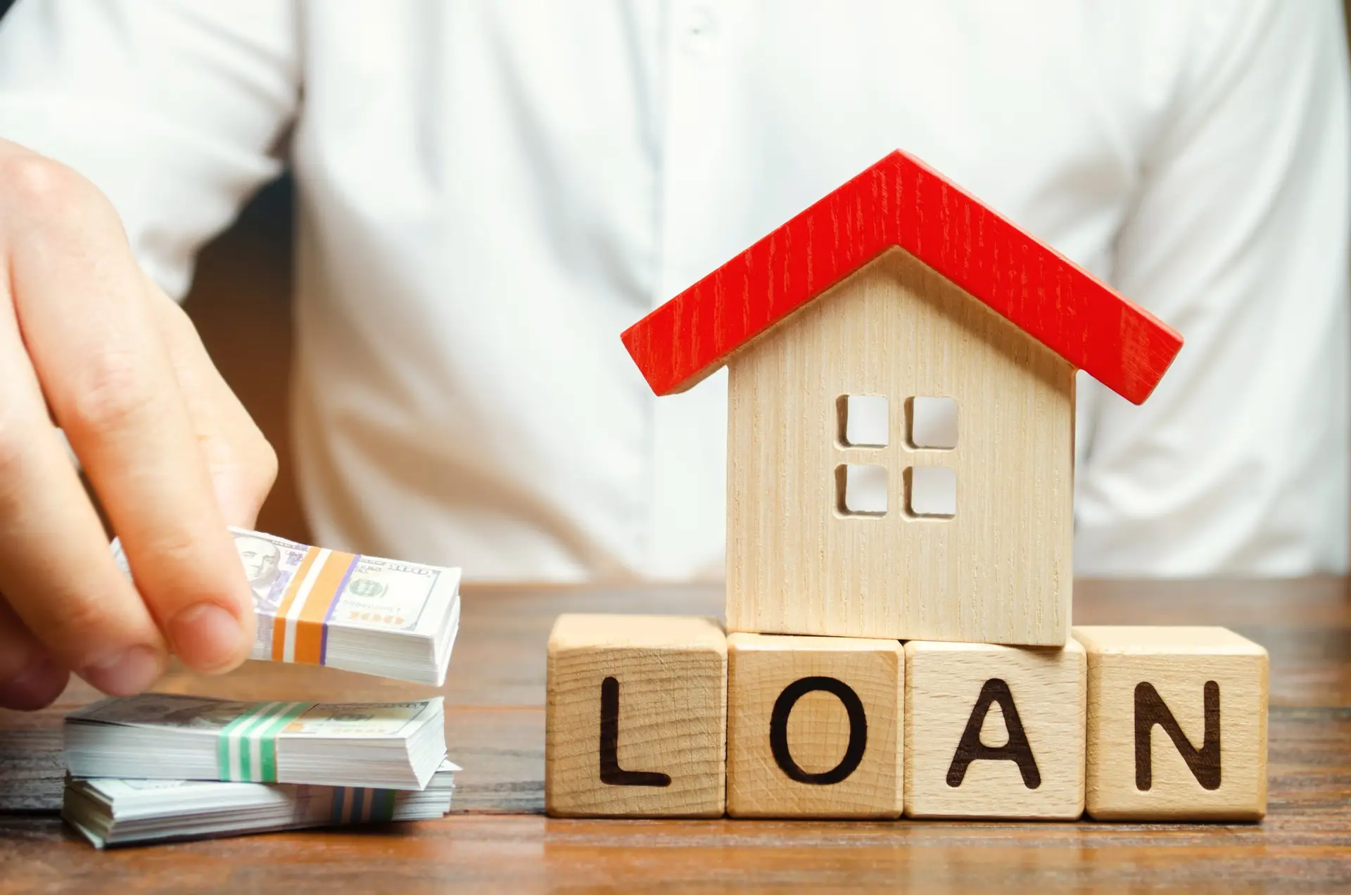 Wooden Blocks With The Word Loan House And Money In The Hands Of A Businessman